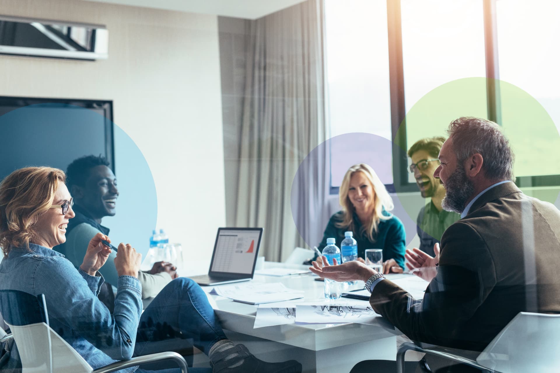 A team laughing together around a meeting table in a bright office with large windows