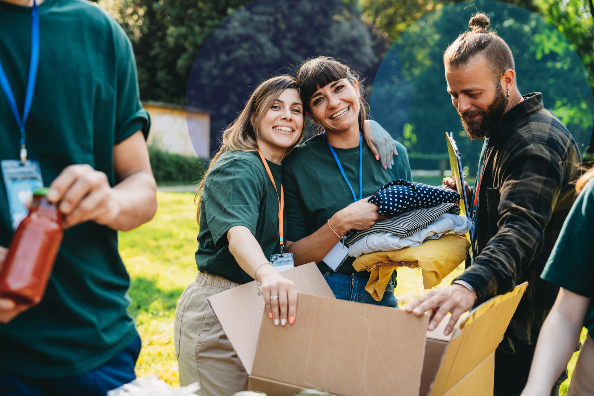 Three smiling volunteers in green shirts packing donated clothes into a cardboard box outdoors