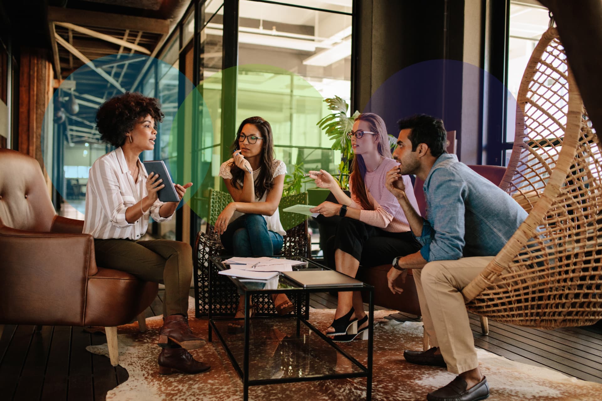 Four people talking around a table in a warm, plant-filled office